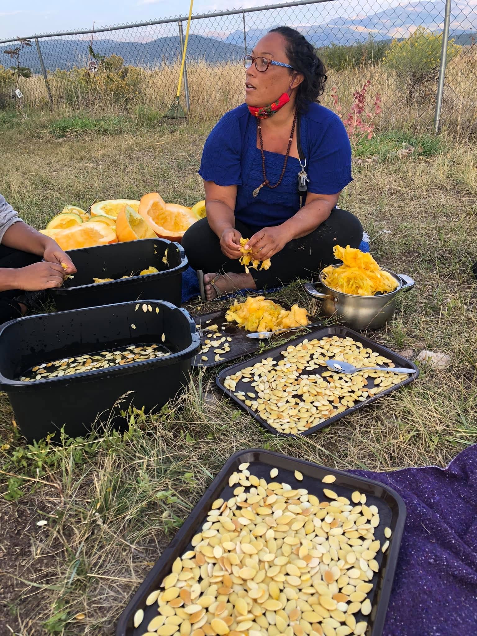 A seedkeeper kneeling with an armful of squash and vegetables from the harvest